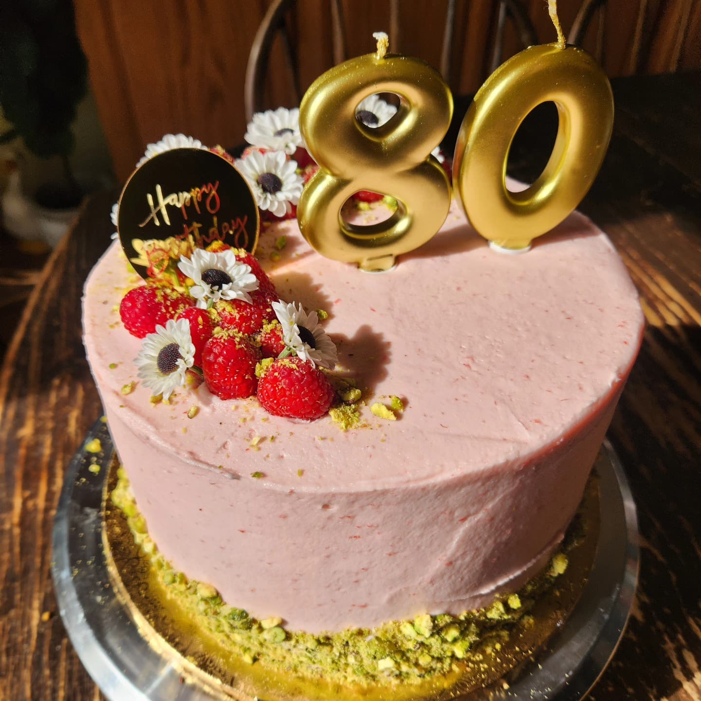 Pink frosted birthday cake with gold number balloons and fresh raspberries